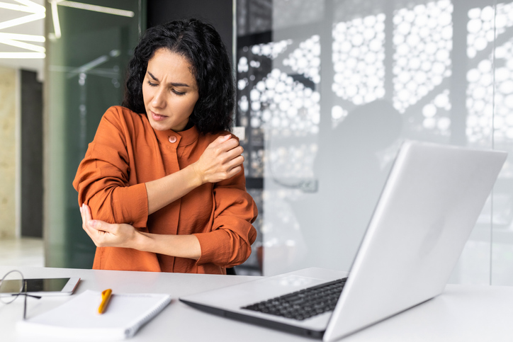 Woman sitting at laptop holding elbow after hitting funny bone